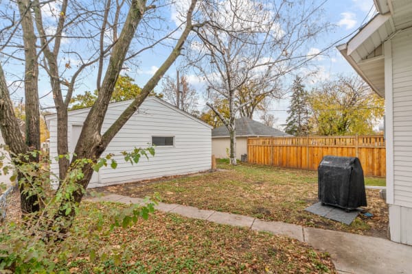 Backyard with a white shed, a large tree with bare branches, a concrete path, and a covered grill.
