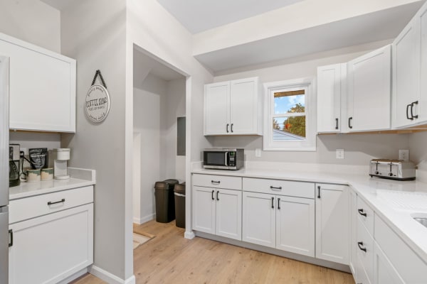 Modern kitchen with white cabinets, coffee bar, and natural light from window.