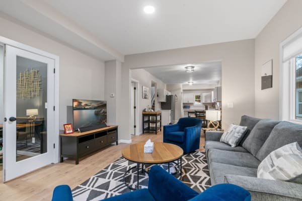 A cozy living room with grey sofa, blue chairs, and an open kitchen area.