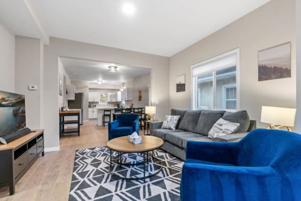 A modern living room with gray sofa, blue armchairs, and open kitchen in the background.