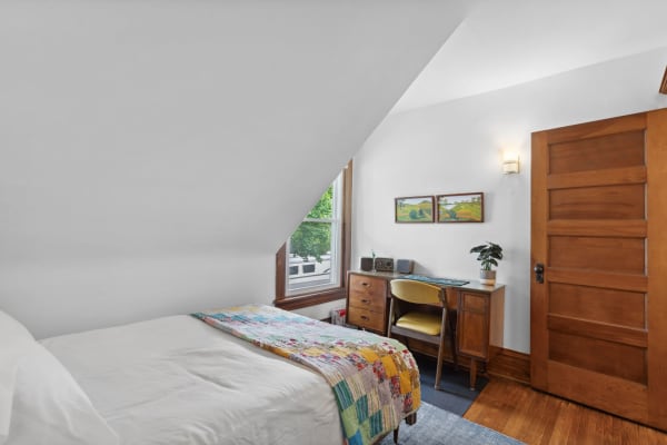 Cozy bedroom with a twin bed, colorful quilt, and wooden desk by a window.