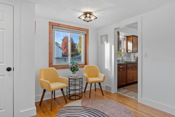 A living area featuring yellow chairs and a view of colorful trees through a window.