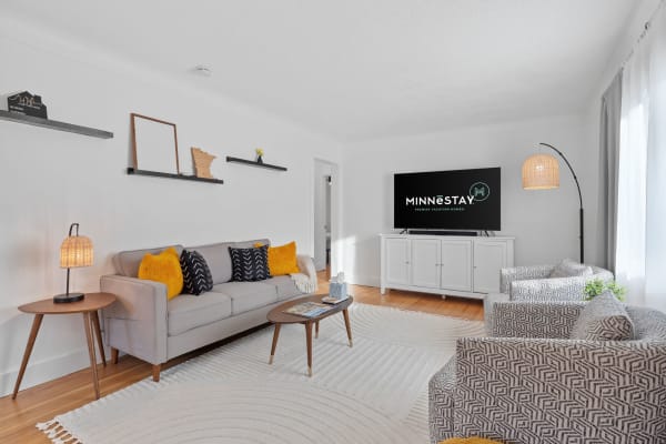 A stylish living room featuring a gray sofa, accent chairs, and a TV with 'Minnestay' branding.