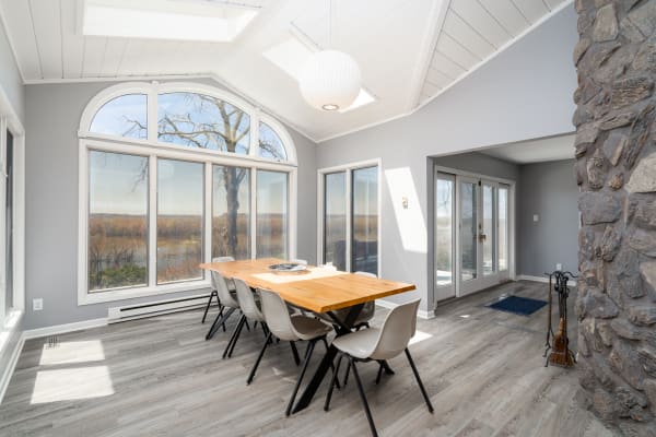 Modern dining room featuring a wooden table, cream chairs, and large windows with views of nature.