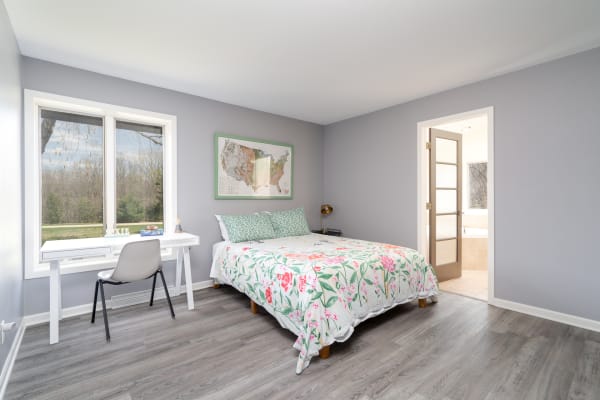 Bedroom featuring a floral quilt on a bed, a desk by a window, and a bathroom doorway.