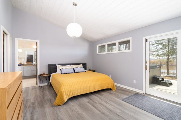 Bright and modern bedroom featuring a mustard quilt and sliding glass door overlooking trees and water.