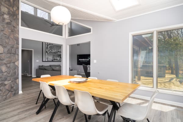 Modern dining area featuring a wooden table and white chairs with a view of the outdoor deck.