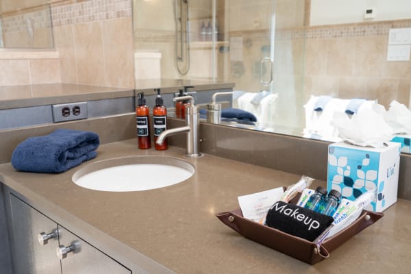 A contemporary bathroom countertop with sink, towels, and various toiletries.