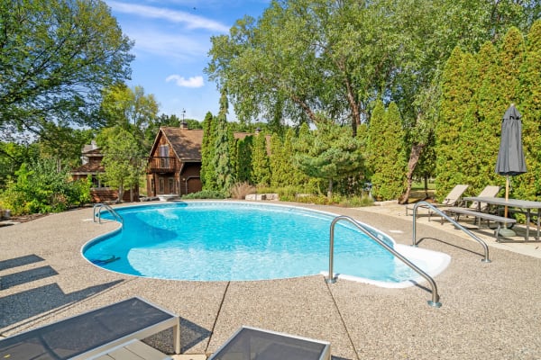A clear swimming pool in a garden with a rustic house in the background.