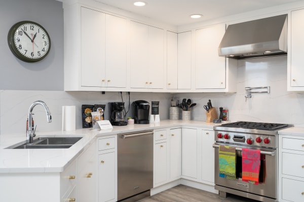 A contemporary kitchen featuring white cabinets, a stainless steel stove, and a round wall clock.