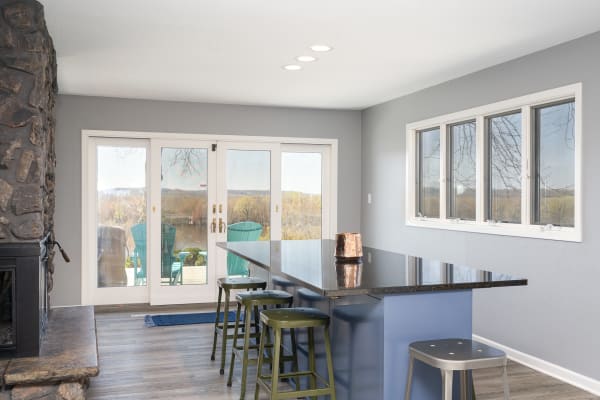 Interior view of a modern kitchen featuring a stone fireplace and a black countertop with bar stools, and a sliding glass door to an outdoor patio.