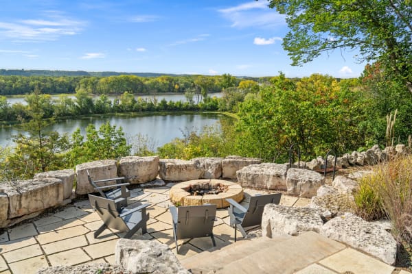 Outdoor fire pit with chairs, overlooking a river and forest.