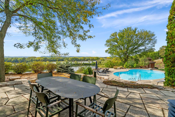 Outdoor dining area overlooking a pool and calm water surrounded by greenery.