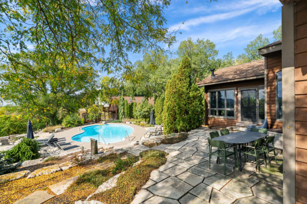 A scenic swimming pool area with lounge chairs and a dining table set amidst trees and shrubs.