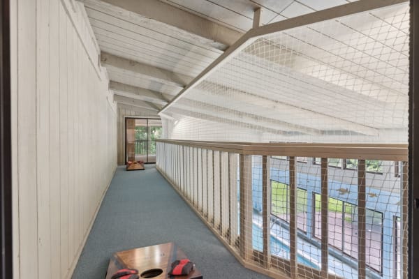 A bright hallway with a sloped ceiling, wooden railing, and cornhole boards on a blue carpet.