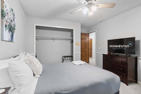 A cozy bedroom with a gray bed, decorative pillows, floral art, and a dresser with a TV.