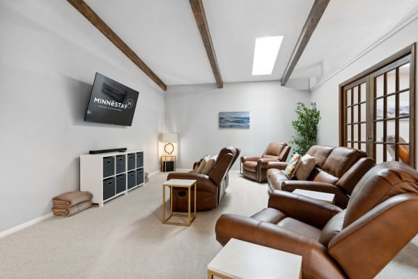 A modern living room with leather recliners, wall-mounted TV, and natural light from a skylight.