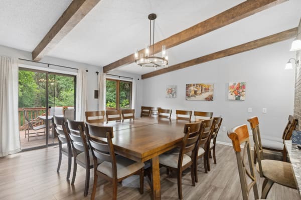 Spacious dining area featuring a large wooden table with matching chairs, a chandelier, and a view of nature through sliding doors.