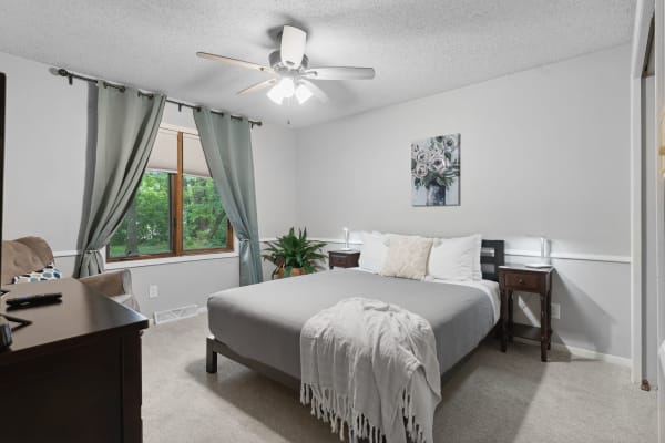 Cozy bedroom with a gray bedspread, a wooden nightstand, and a framed artwork of flowers.