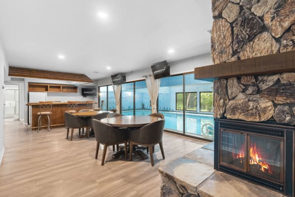 An elegant indoor area with a bar, dining table, and an indoor swimming pool visible through large windows.