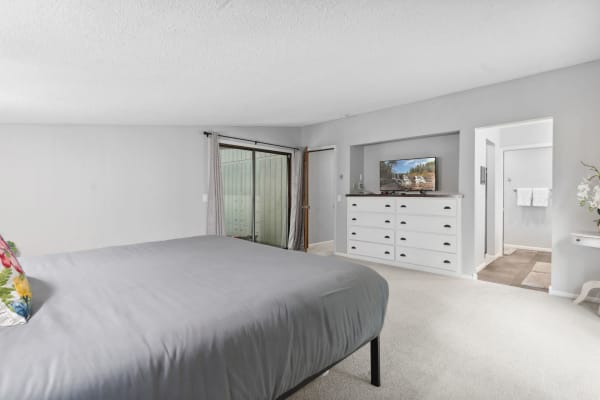 A spacious bedroom featuring a large bed, a wall-mounted TV, and access to an outdoor space.