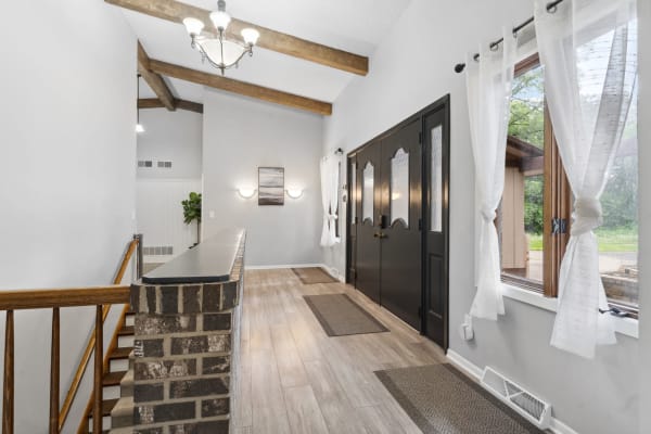 Entryway with high ceilings, wooden beams, double black doors, and light-colored flooring.
