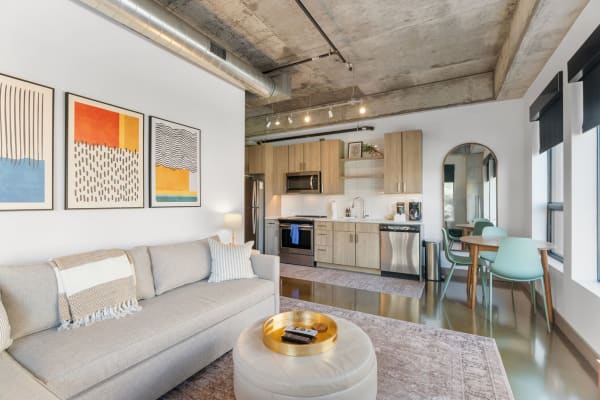 Stylish living room and kitchen of a modern apartment with a gray sofa, abstract art, and mint-green dining chairs.