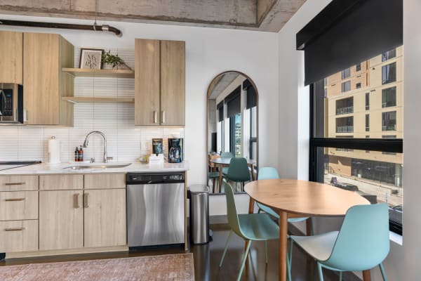 Interior view of a modern kitchen with light wooden cabinets and a dining area near the window.