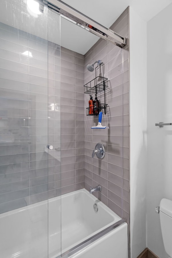 A contemporary shower area featuring a glass door, gray tiles, and a white bathtub.