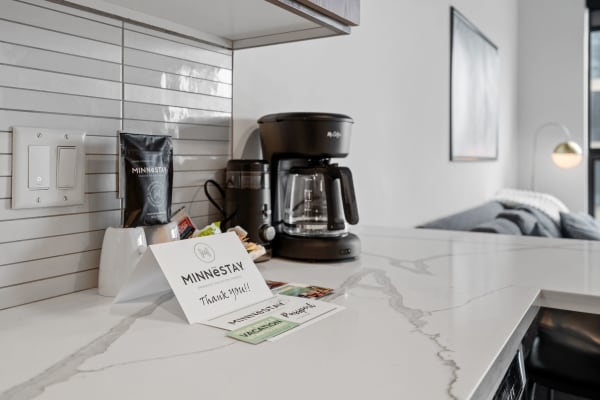 A modern kitchen countertop featuring a coffee maker and a welcoming note card.