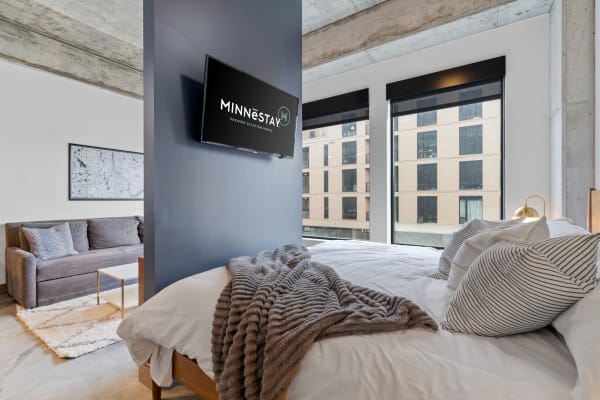 Contemporary studio apartment featuring a cozy bed, sofa, and large windows with urban views.
