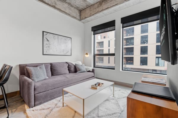 Modern living room with gray sofa, coffee table, and large windows overlooking a building.