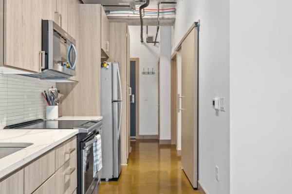 Interior view of a modern kitchen with light wood cabinets and a hallway.