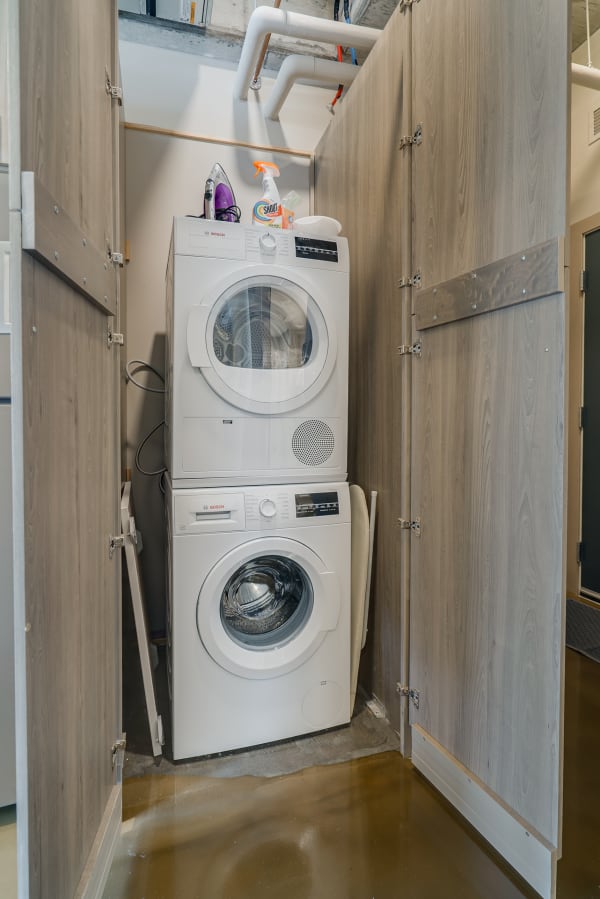 Stacked Bosch washer and dryer in a laundry closet, with cleaning supplies on top.
