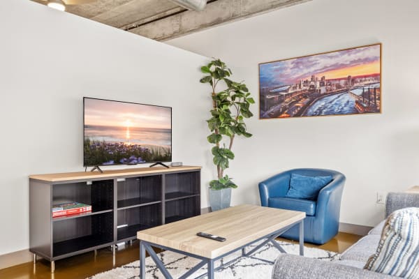 A stylish living room with a blue armchair, coffee table, and a large TV displaying a sunset.