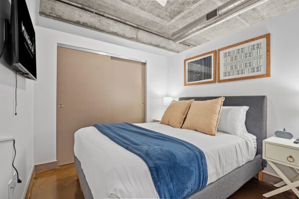 A contemporary bedroom with a neatly made bed, nightstand, and framed art on the wall.
