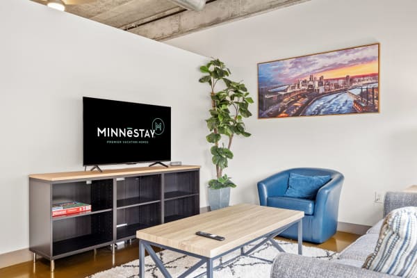 Contemporary living room with a TV, plant, blue armchair, and city skyline artwork.
