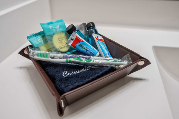 A brown tray filled with cleansing wipes, shampoo bottles, toothpaste, a toothbrush, and a navy towel labeled 'Cosmetic.'