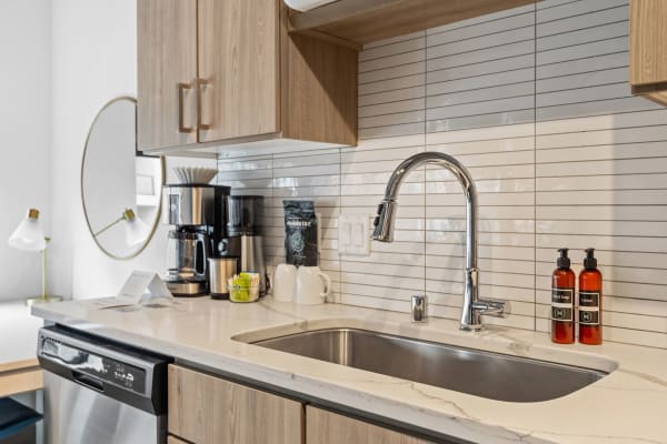 Modern kitchen countertop with stainless steel sink, coffee maker, and stylish products.