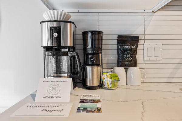 A coffee station with a drip coffee maker, a single-serve machine, coffee bags, mugs, and sugar packets.
