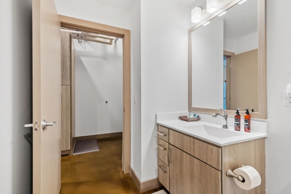 Modern bathroom featuring a wooden vanity, mirror, and a doorway leading to another room.