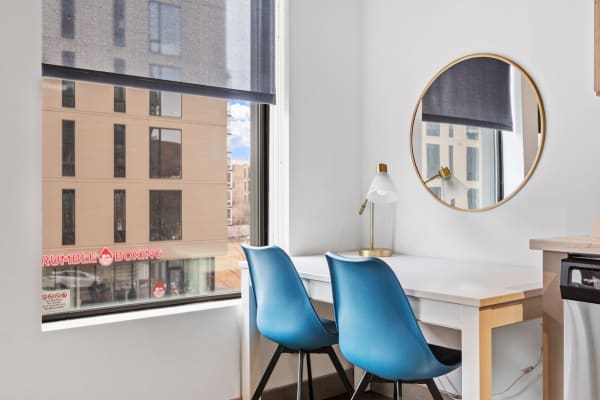 Modern workspace featuring a white desk, blue chairs, and a round gold-framed mirror by a large window.