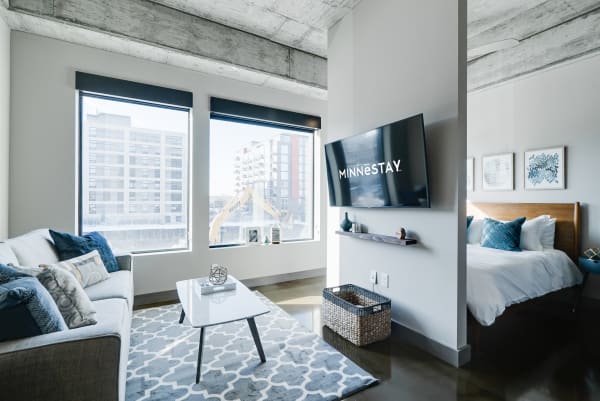 Modern apartment interior with sectional couch, coffee table, TV, and bedroom area.