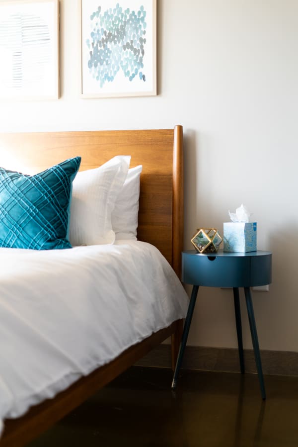 A cozy bedroom with a wooden bed, turquoise pillow, and blue side table with decor items.