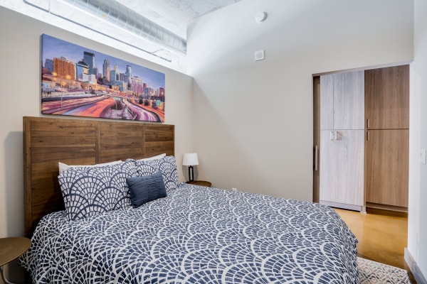 Cozy bedroom with a wooden headboard, patterned bedspread, and a city skyline painting.