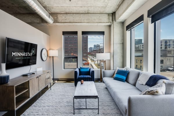 Modern living room with large windows, grey sofa, blue armchair, and TV unit.