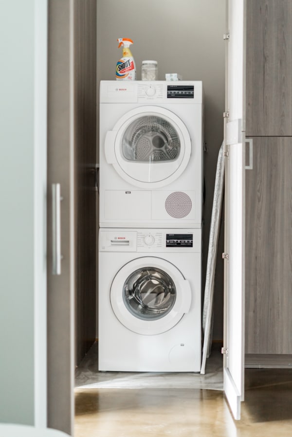 A compact laundry area with stacked Bosch washing machine and dryer, cleaning supplies on top.