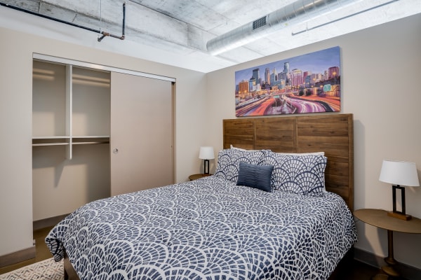 Cozy bedroom with a bed, wooden headboard, patterned bedding, and city skyline artwork.