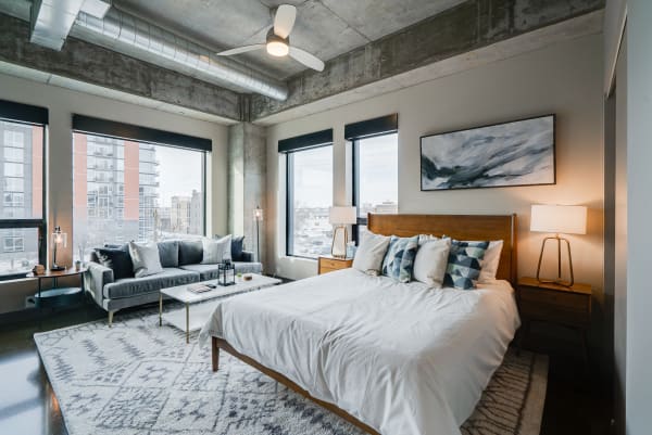 A bright, modern bedroom with a concrete ceiling, large windows, and stylish furniture.