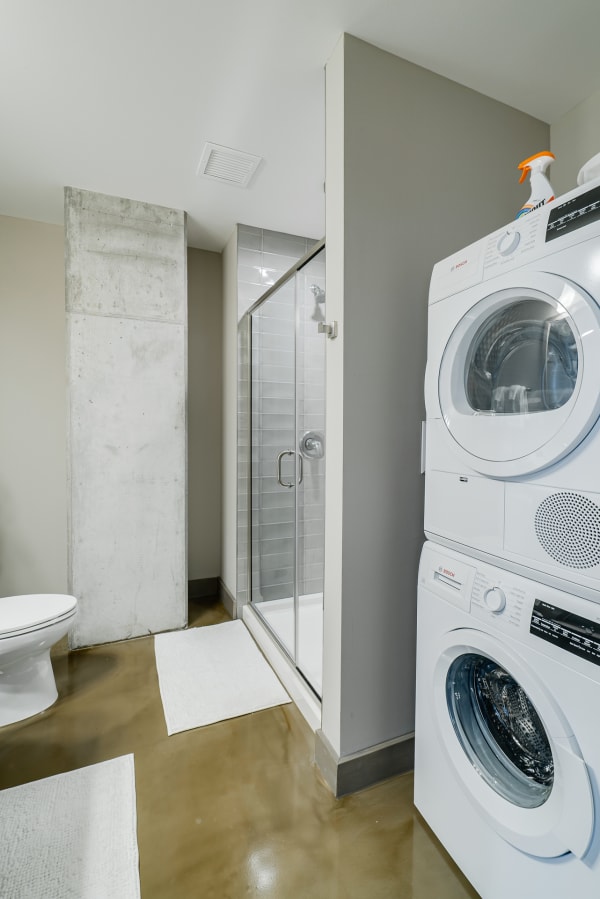 Interior view of a contemporary bathroom with a shower, toilet, and washer-dryer unit.